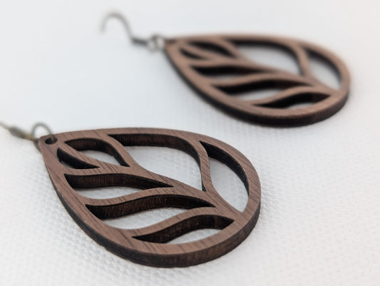 Dark brown walnut wood teardrop earrings with an open leaf design, shown on a textured white background.