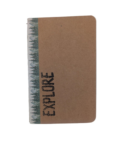 A small kraft paper notebook with rounded corners, featuring a vertical black 'EXPLORE' text print on the front and a patterned spine with dark green trees on a white background.